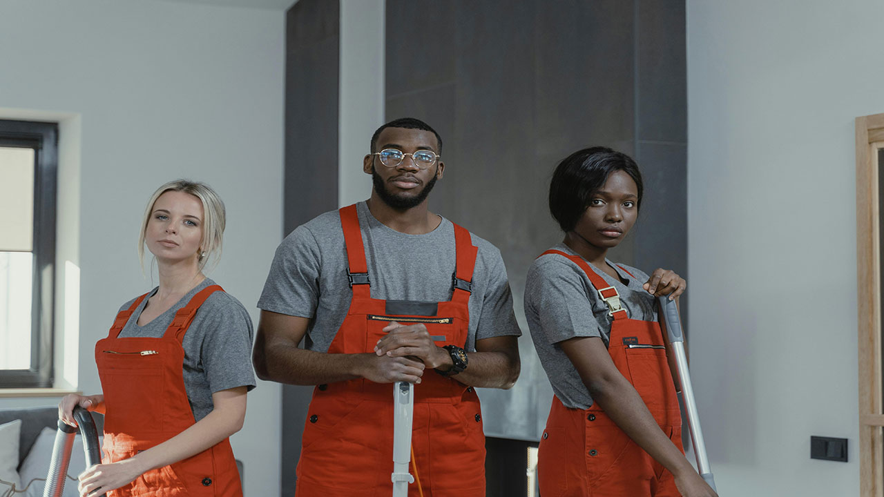 Two female and one male cleaner holding cleaning gadgets, standing together.