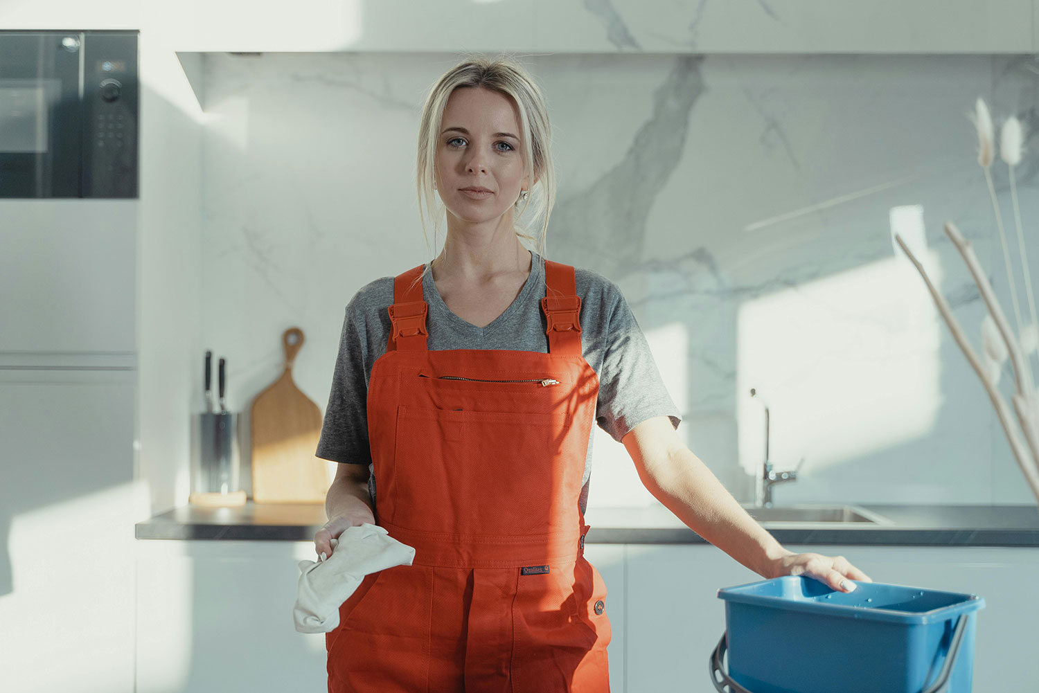 Female cleaner holding a blue bucket with cleaning supplies.