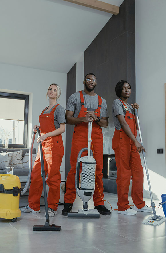 A professional cleaning team in red uniforms with vacuum and mop equipment, standing in a modern living room.