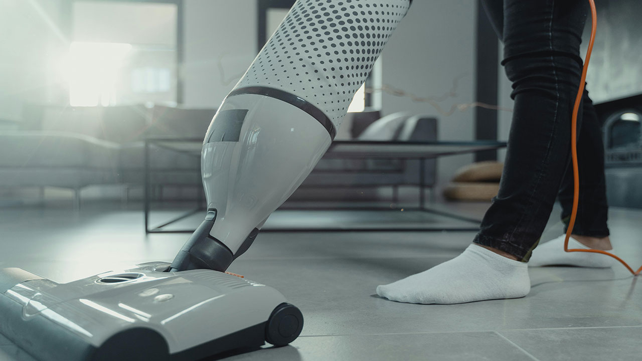 Modern vacuum cleaner being used to clean a tiled floor in a contemporary living room.